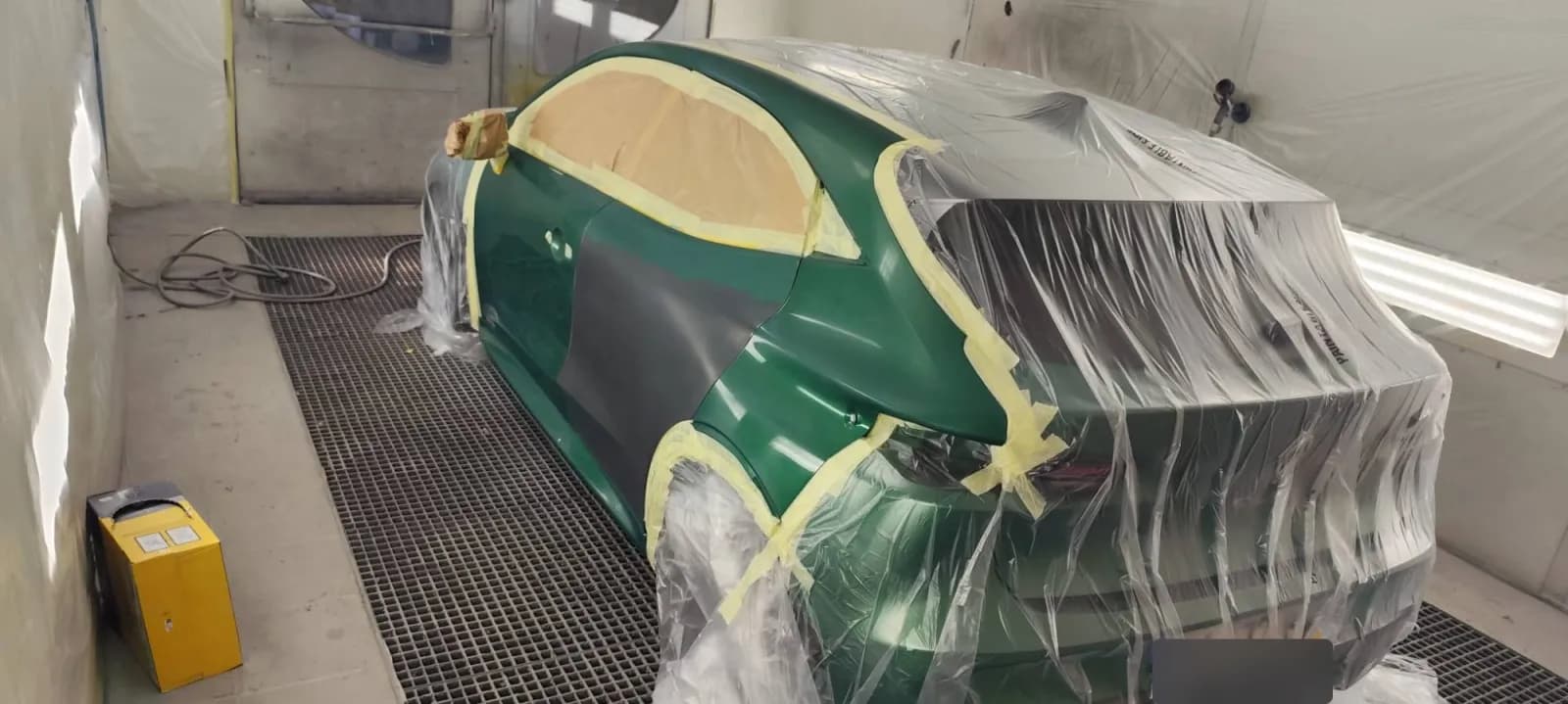 Renault Clio 6 verte en cabine, porte arrière gauche en apprêt gris, véhicule masqué sous film