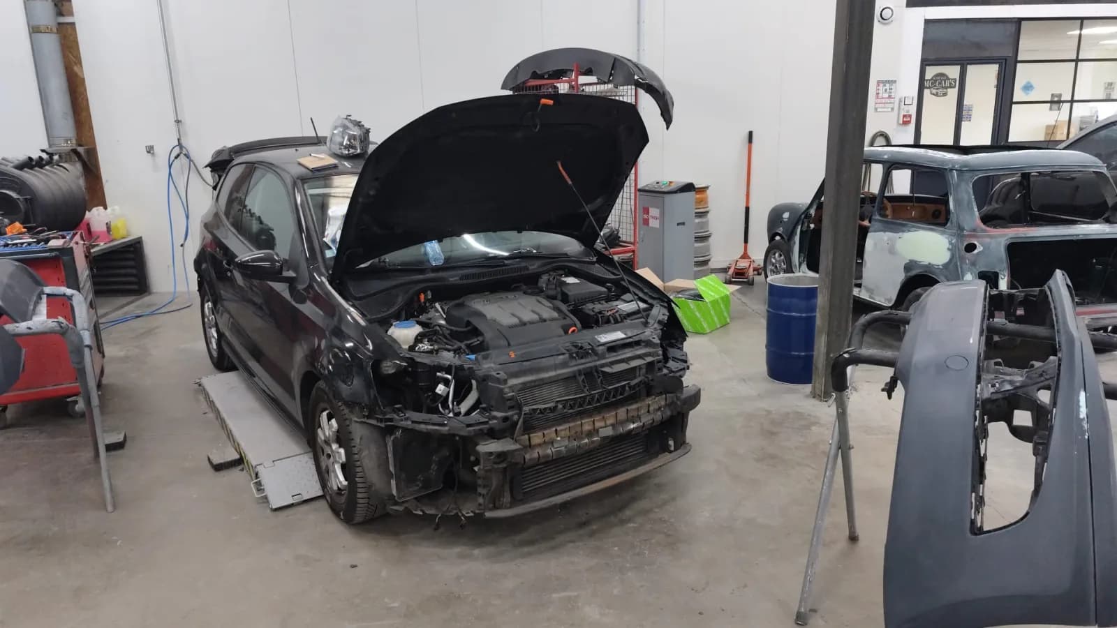 Volkswagen Polo noire en atelier, avant déposé : pare-chocs et phare retirés, face avant à nu, capot ouvert