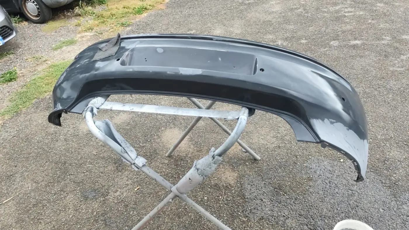 Pare-chocs de Volkswagen Polo noir posé sur un tréteau, en préparation avant peinture