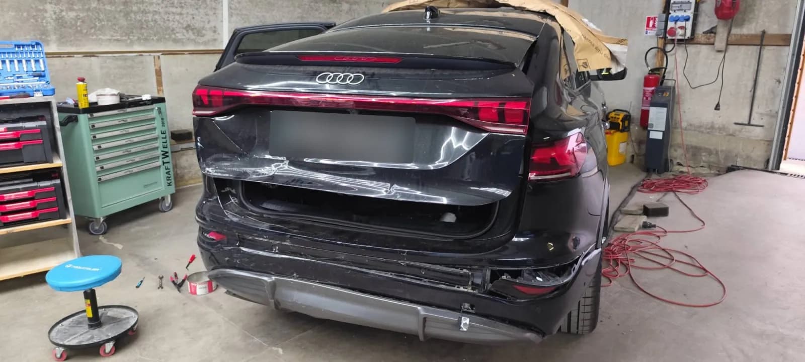 Audi Q6 noire à l'arrivée, vue arrière : hayon enfoncé et pare-chocs arrière arraché côté droit, plaque masquée