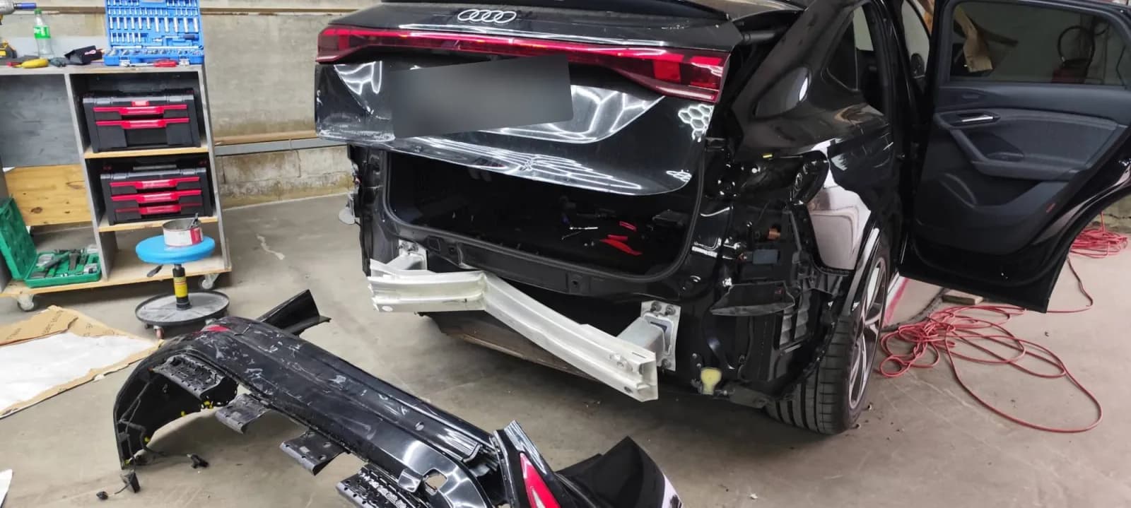 Audi Q6 arrière déposé : pare-chocs au sol, traverse arrière tordue visible, plaque masquée