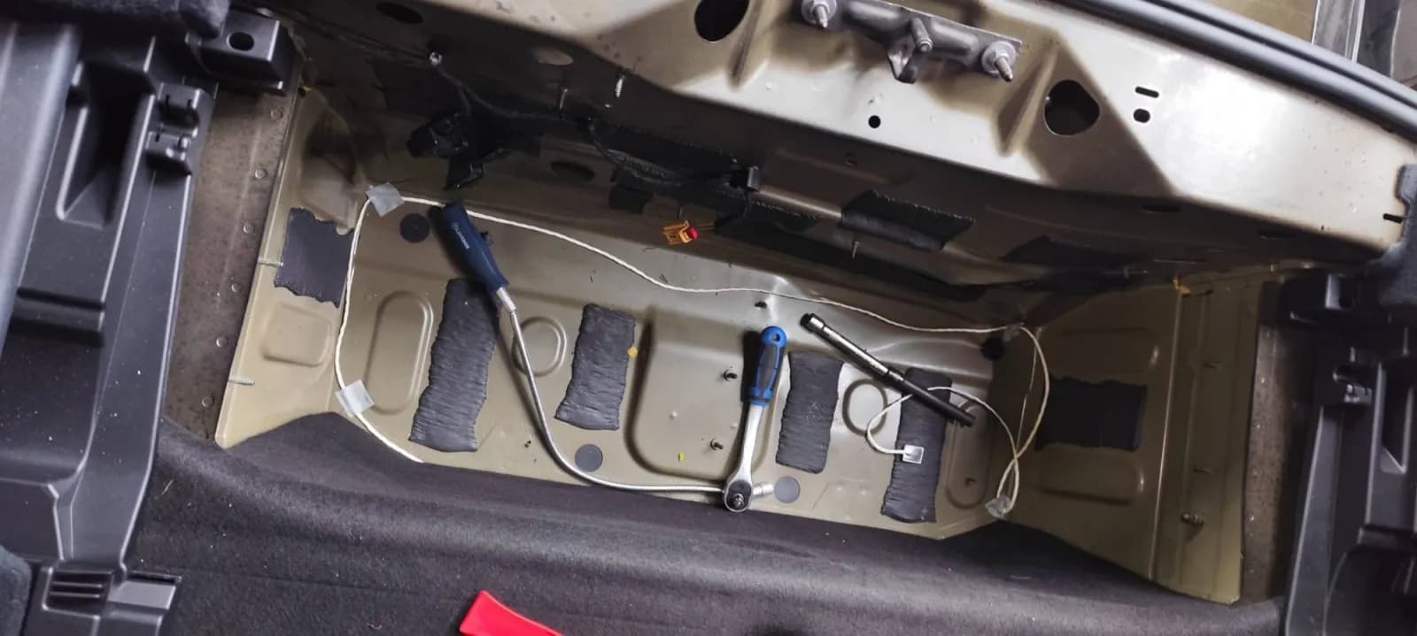 Plancher arrière d'Audi Q6 mis à nu, garnitures déposées, outils posés sur la tôle