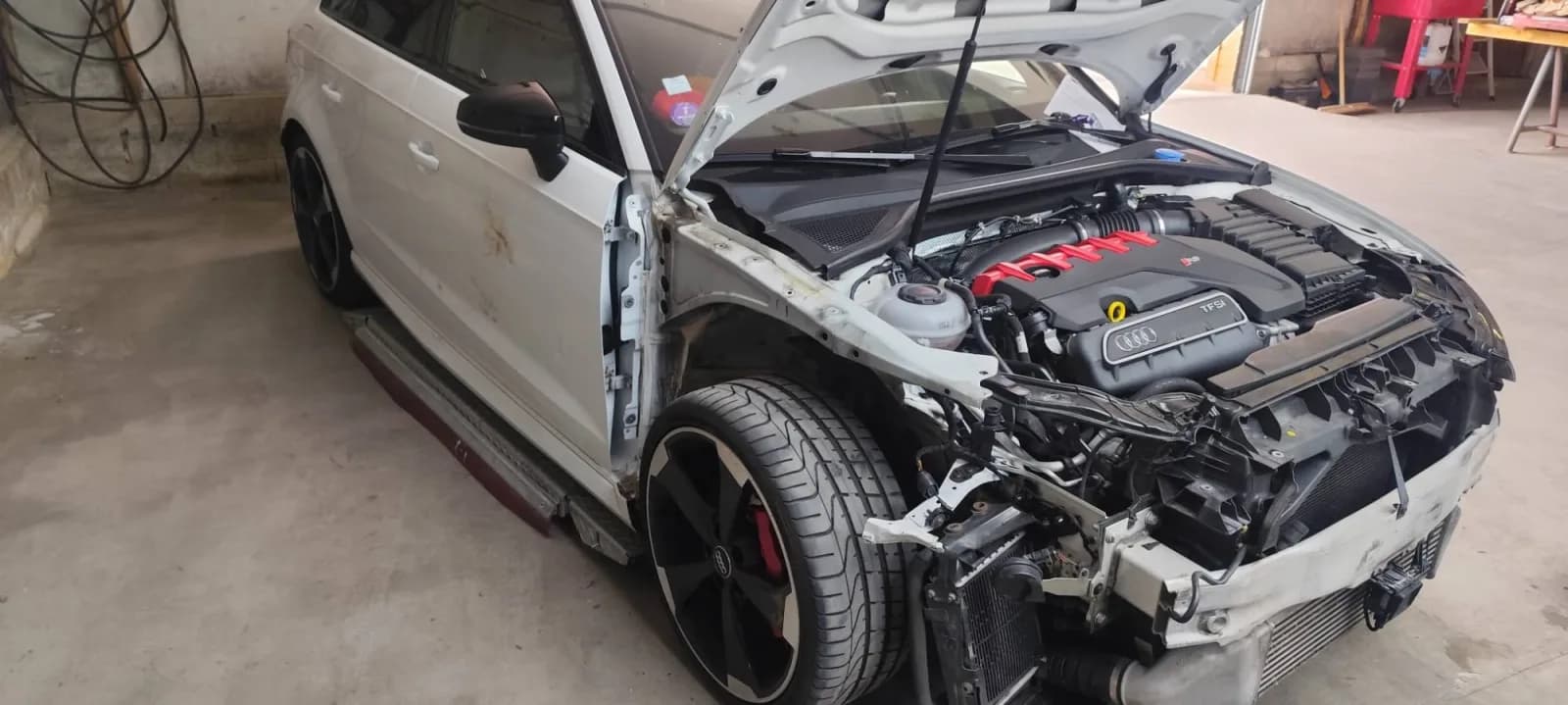 Audi RS 3 à l'aile avant droite déposée, structure du pied avant mise à nu, capot ouvert