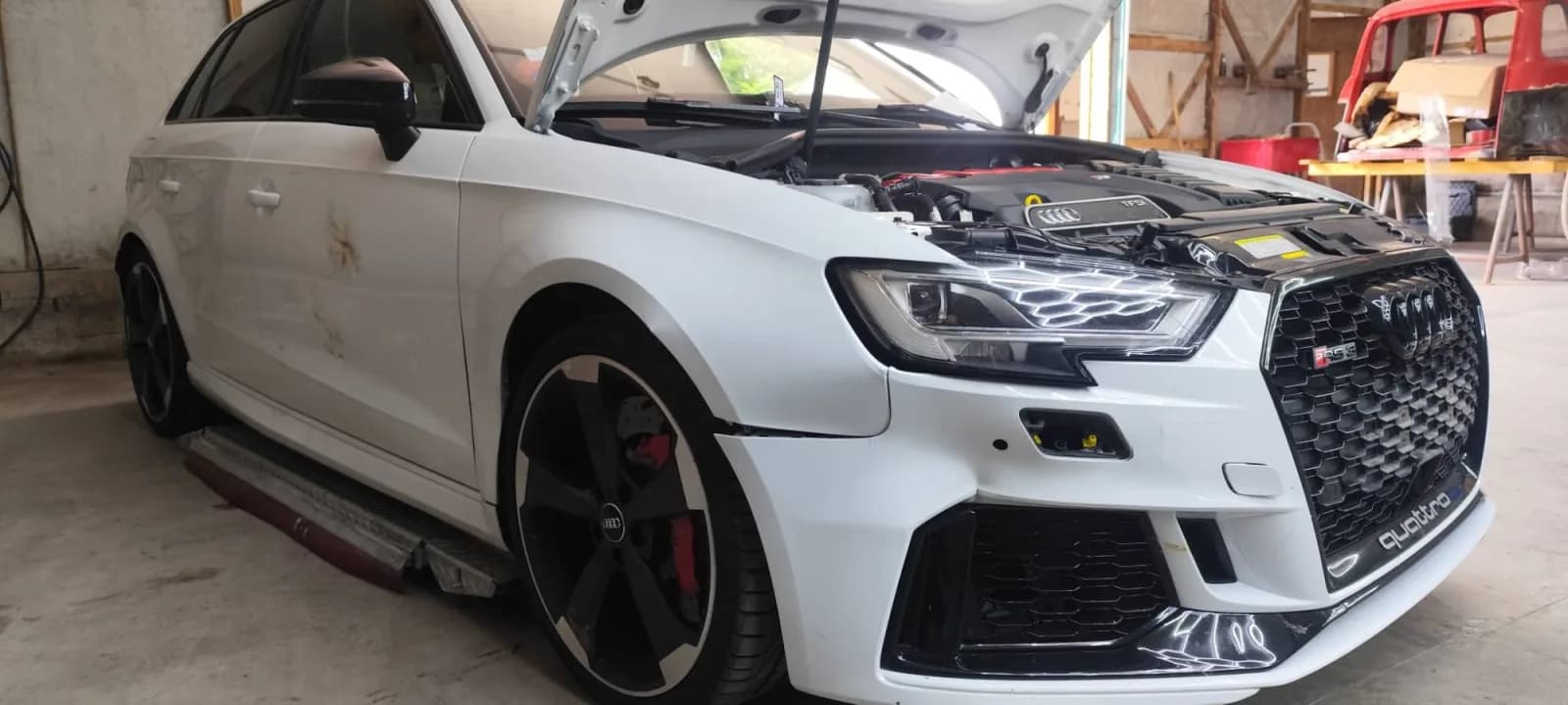 Audi RS 3 en cours de remontage, face avant, calandre et optique avant droite neuve reposées, capot ouvert
